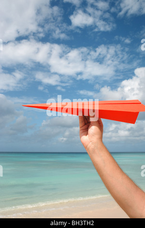 Eines Mannes Hand, die einen Flieger in der Luft auf einem einsamen tropischen Strand Stockfoto