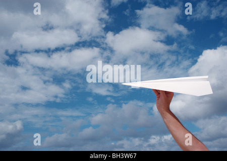 Eines Mannes Hand hielt eine weißes Papierflugzeug in blau bewölktem Himmel Stockfoto