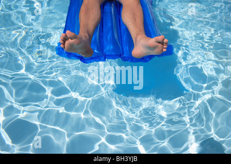 Nahaufnahme eines Mannes Beine und Füße entspannen Sie sich auf eine aufblasbare Lilo Luftmatratze schwimmend in einem Schwimmbad mit blauem Wasser Stockfoto