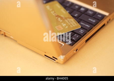 Ein goldener Laptop-Computer und eine goldene Kreditkarte auf einem goldenen Tisch Stockfoto