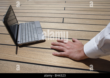 Die Hand eines Mannes ruht neben einem Netbook-Computer auf einem Holzdeck Stockfoto