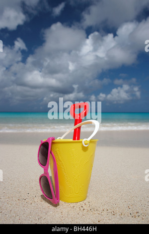 Ein gelber Eimer, Spaten und eine Sonnenbrille auf einem einsamen tropischen Strand Stockfoto