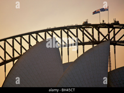 Blick auf Menschen touring die Struktur der Sydney Harbour Bridge bei Sonnenuntergang mit Opernhaus von Sydney im Vordergrund. Stockfoto