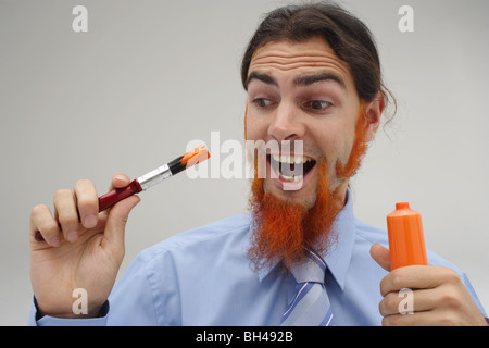 Ein junger Geschäftsmann seinen Bart mit orange Farbe malen, lachen Stockfoto