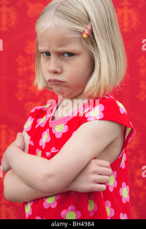 Junges Mädchen in einem roten Kleid stehend mit ihre Arme gefaltetes Stirnrunzeln mit einem miserablen Ausdruck gegen rote Tapete Stockfoto
