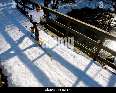 Ein junger Mann Langlaufski auf einem Weg über eine Brücke in Anchorage, Alaska. Stockfoto