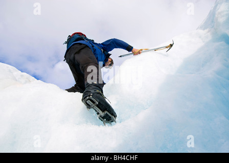 Ein junger Mann klettert Schritte auf einem Gletscher mit Steigeisen und Eispickel in Franz Josef, Neuseeland. Stockfoto