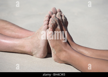 Ein Mann und eine Frau drücken ihre Füße gegeneinander auf einem sandigen Strand liegend Stockfoto