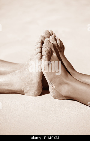 Ein Mann und eine Frau drücken ihre Füße gegeneinander auf einem sandigen Strand liegend Stockfoto