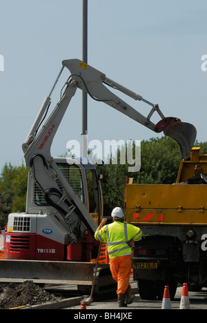 Bauarbeiter graben ein Pflaster mit einem überwachten Aushub Maschine, Aberystwyth, Wales. Stockfoto