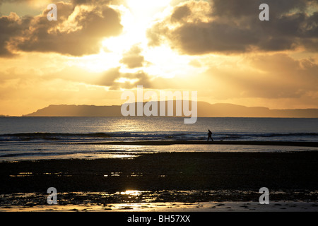 Mann zu Fuß einen kleinen Hund auf Glenbrittle Strand, mit den Sonnenuntergang über der Insel Rum in der Ferne, Isle Of Skye, Schottland Stockfoto