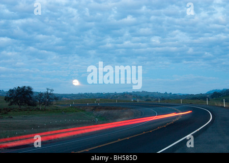 Eine Straße in der Nacht mit den Mondaufgang und Scheinwerfer und Tail helle Streifen Stockfoto