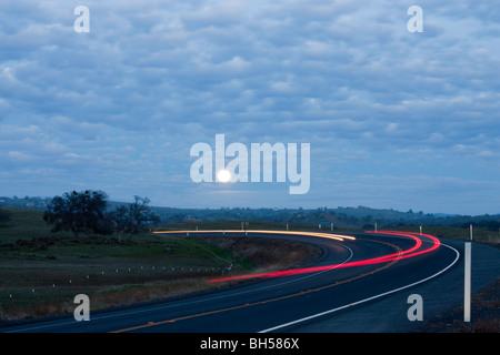 Eine Straße in der Nacht mit den Mondaufgang und Scheinwerfer und Tail helle Streifen Stockfoto