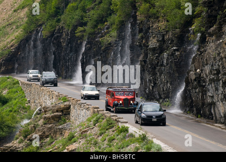 Fahrzeuge, darunter ein "Red Bus' on Going to the Sun Road durchqueren Wasserfall, bekannt als die"Weeping Wall" Stockfoto