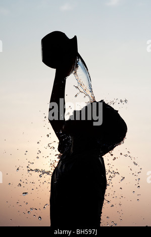 Indischer junge gießt Wasser auf sich selbst aus einem Tontopf Silhouette. Andhra Pradesh. Indien Stockfoto