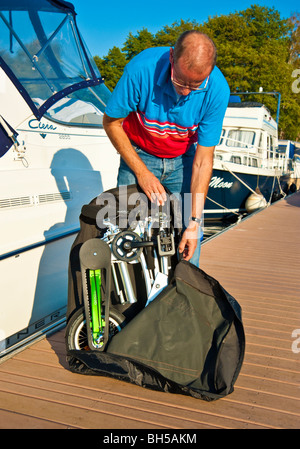 Mann, die Entfaltung einer Mobiky Klapprad auf einem Bootssteg mit Yachten Stockfoto