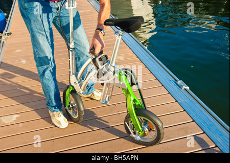 Mann, die Entfaltung einer Mobiky Klapprad auf einem Bootssteg mit Yachten Stockfoto