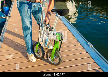 Mann, die Entfaltung einer Mobiky Klapprad auf einem Bootssteg mit Yachten Stockfoto