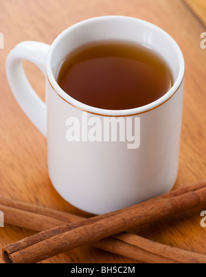 Eine Tasse Tee oder Apple Cider auf einem Tisch hinter ein paar Zimtstangen. Stockfoto