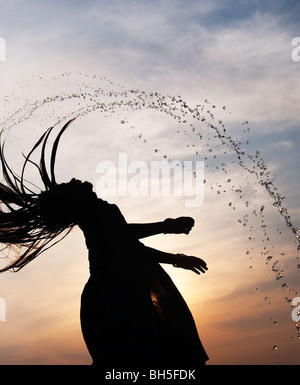 Indisches Mädchen werfen ihre nassen Haare zurück, wodurch Wasser spray Silhouette. Andhra Pradesh, Indien Stockfoto