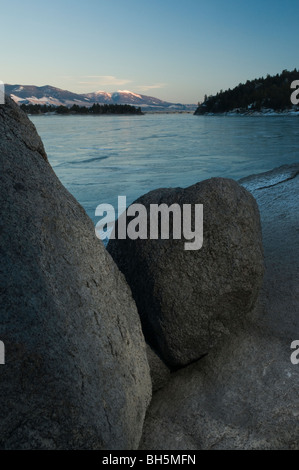 schneebedeckten MTS Edith und Baldy umrahmt von Granitfelsen auf eisigen Canyon Ferry Reservoir Stockfoto