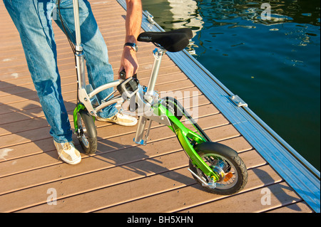 Mann, die Entfaltung einer Mobiky Klapprad auf einem Bootssteg mit Yachten Stockfoto