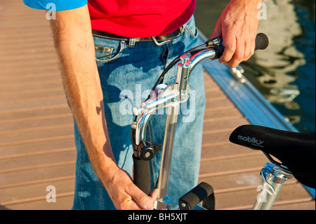 Mann, die Entfaltung einer Mobiky Klapprad auf einem Bootssteg mit Yachten Stockfoto