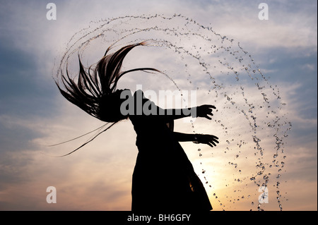 Indisches Mädchen werfen ihre nassen Haare zurück, wodurch Wasser spray Silhouette. Andhra Pradesh, Indien Stockfoto