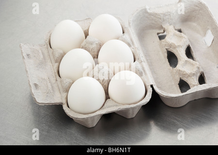 Sechs weiße Hühnereier in einem Karton auf einer zerkratzten Metallfläche. Stockfoto