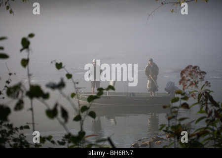 ZWEI FISCHER IM BOOT ANGELN IM FLUSS BODENNEBEL SCHLECHTES WETTER AM FRÜHEN MORGEN KEIN MODEL RELEASE Stockfoto