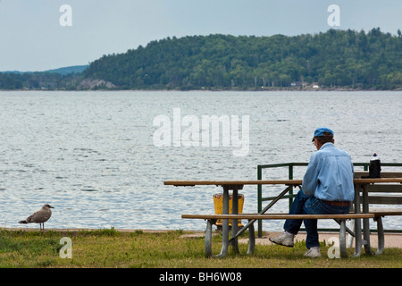 Ein Mann, der auf einer Bank am Seeufer in den USA sitzt US-Lifestyle Alltagsleben Szenen des Lebens Konzept Ereignisse horizontal Hi-res Stockfoto