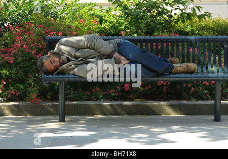 Ein obdachloser Mann schlafen auf einer öffentlichen Bank in einem Stadtpark Stockfoto