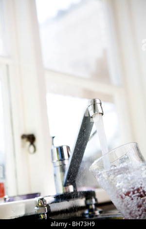 Kaltes Wasser aus dem Wasserhahn läuft in ein Trinkglas. Stockfoto