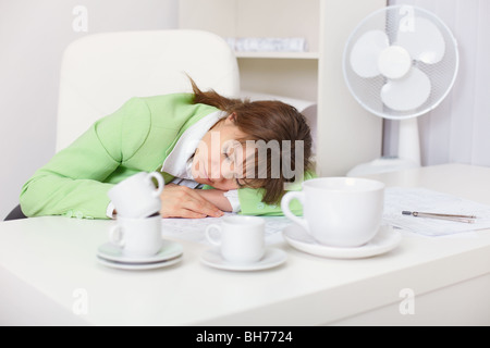 Müde Frau schläft auf dem Schreibtisch im Büro unter die Kaffeetassen Stockfoto