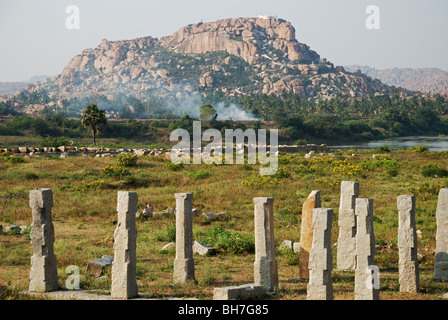 Alte Brücke in Schutt und Asche mit dem Fluss und einem felsigen Hügel im Hintergrund. Hampi, Indien. Stockfoto