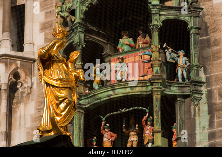 Goldene Statue der Jungfrau Maria schimmert in der Sonne neben berühmten Glockenspiel Rathaus München Stockfoto