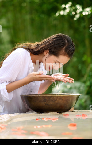 Junge Frau spritzt sich Wasser auf ihr Gesicht Stockfoto