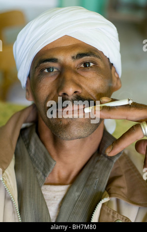 Porträt eines arabischen muslimischen ägyptischen Mann, ein Kopftuch zu tragen und das Rauchen einer Zigarette, in der Sahara in der Dakhla Oase, Western Desert, Ägypten. Stockfoto