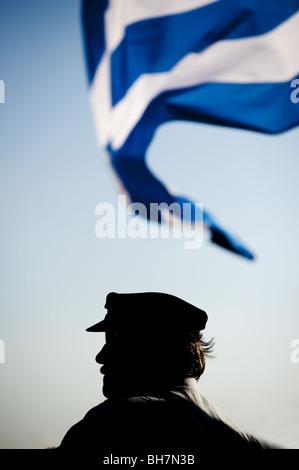 Griechischer Mann auf Fähre unter griechischer Flagge Wind geblasen. Stockfoto