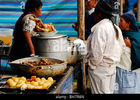 Ecuador, Otavalo, Seitenansicht des indigenen Mann mit langen Haaren geflochten und eine Frau stehen in einem Stall mit Bratkartoffeln, tief Stockfoto