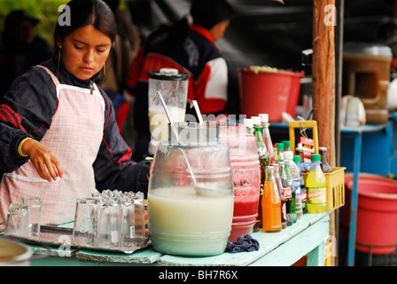 Ecuador, Otavalo, junge Frau trägt ein Licht rosa Dienstmädchen Schürze stehen am Marktstand Lebensmittel Getränke in Gläsern Stockfoto