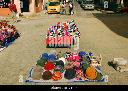 Ecuador, Otavalo, Hüte auf dem Display an einem bunten Stall in einem Straßenmarkt mit einigen Häusern im Hintergrund Stockfoto