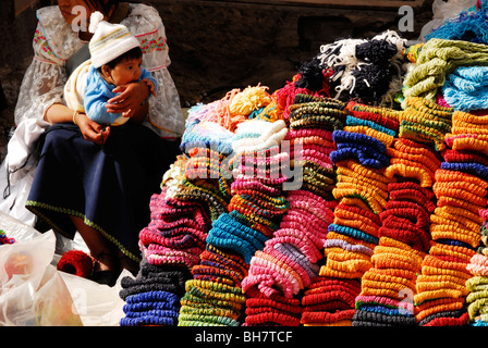 Ecuador, Otavalo, Stapel von bunten wollene Kleidung auf dem Display in einem Straßenmarkt, eine Frau, die einheimische Tracht Stockfoto