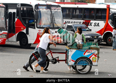 Ecuador, Otavalo, junge Frauen schieben ein Dreirad voller Gasflasche während ein Mädchen sitzen sie mit Busse geparkt Stockfoto