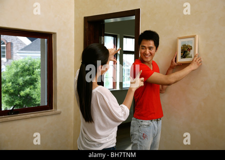 Chinesische junge Paar einen Bilderrahmen an der Wand aufhängen Stockfoto