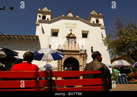 Ecuador, Cuenca, Menschen sitzen auf einer roten Bank in der Nähe von Blumenmarkt, vor ihnen mit Blick auf das Kloster von El C Stockfoto