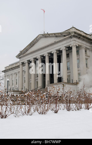 Treasury Building Snow Washington DC // WASHINGTON DC, USA – die Nordfront des Treasury Building in Washington DC, mit einer frischen Schneedecke im Vordergrund. Die ikonische neoklassizistische Architektur hebt sich von der weißen Winterlandschaft ab, in der die amerikanische Flagge über dem Gebäude thront. Stockfoto