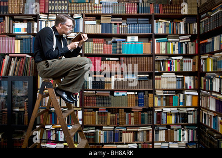 Ein Mann sitzt auf einer Leiter in einer Buchhandlung ein Buch zu lesen Stockfoto