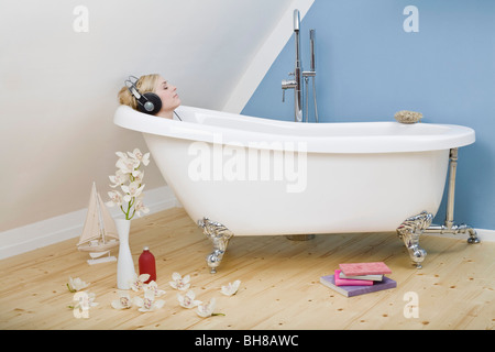Eine Frau entspannend in einer Clawfoot Wanne Kopfhörer anhören Stockfoto