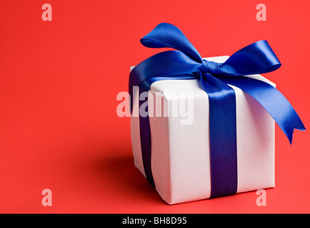 weiße Geschenk mit einem blauen Band auf rotem Grund Stockfoto